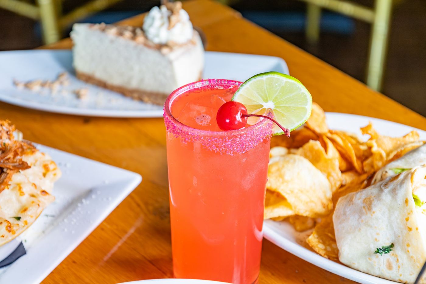 A pink cocktail with a sugar rim, lime and cherry