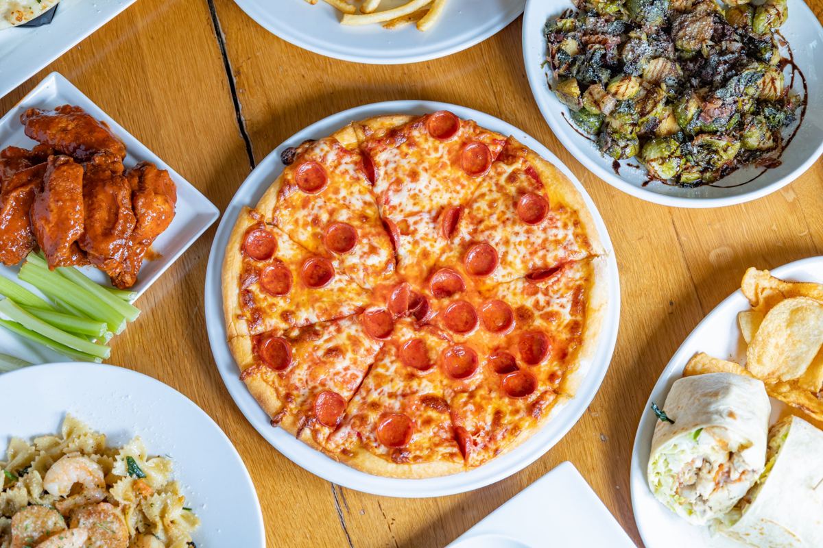 A table of pizza, wings, pasta and Brussels sprouts